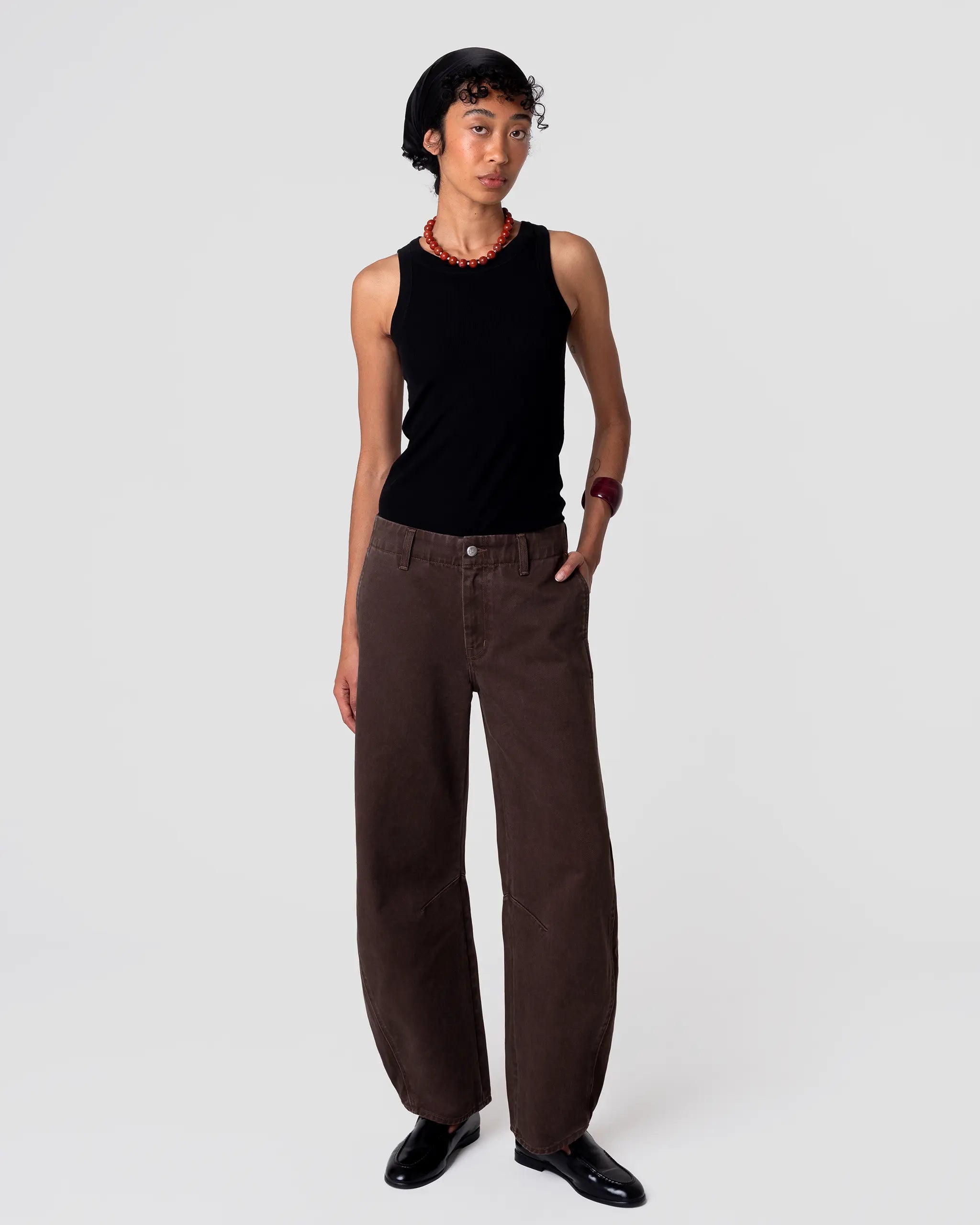 Oketo Cut 103 Barrel Jean in espresso: curved leg, cropped hem, crisp midweight denim; relaxed fit shown from the front, hand in pocket. Pleated hem detail at cuff adds volume.