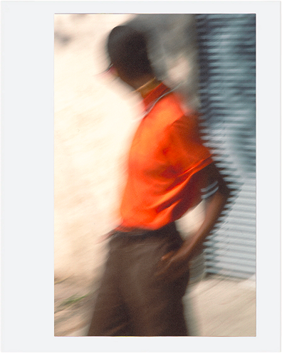 Blurred view of dark denim pants; straight cut, mid-rise, deep indigo tone with minimal visible texture; hand in pocket.