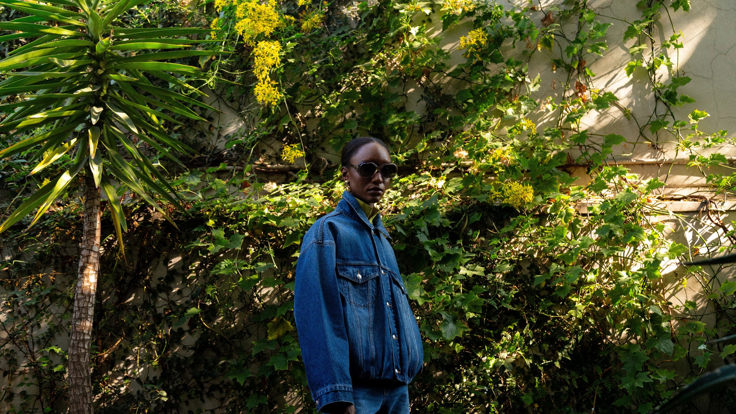 Person wearing a blue denim jacket standing among greenery
